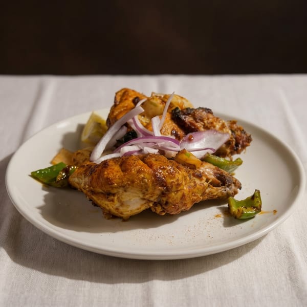 Chicken tikka with red onions, green peppers, and lemon wedges on a white plate.